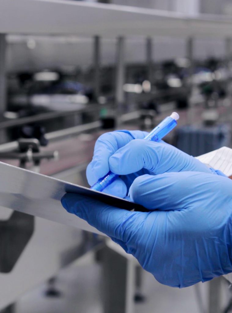 Blue-gloved GMP technician writing during quality control
